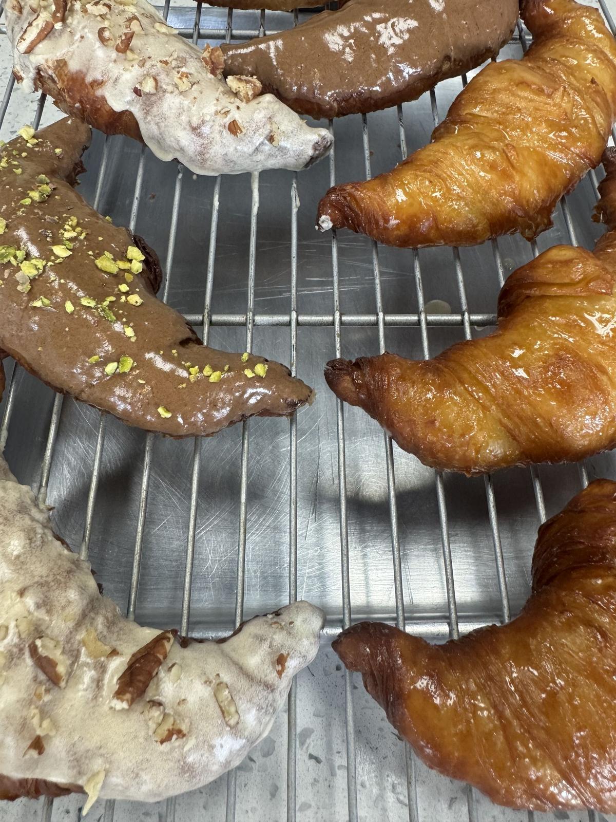 Fresh glazed and pistachio croissants cooling on a rack at B&B Coffee